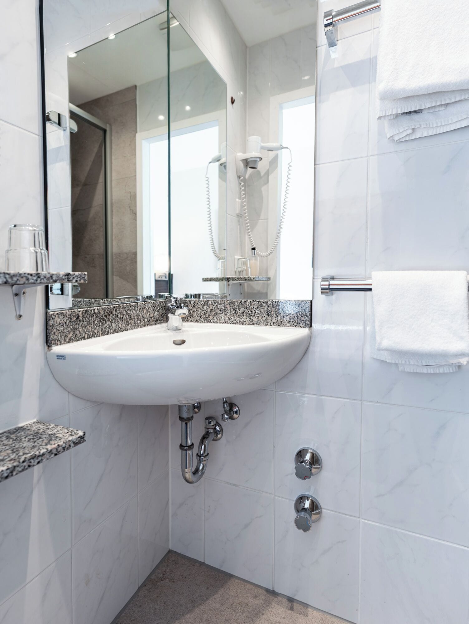 Ein modernes Badezimmer mit einem weißen Waschbecken, einer Duschkabine aus Glas und einer Wand mit Marmorplatten.