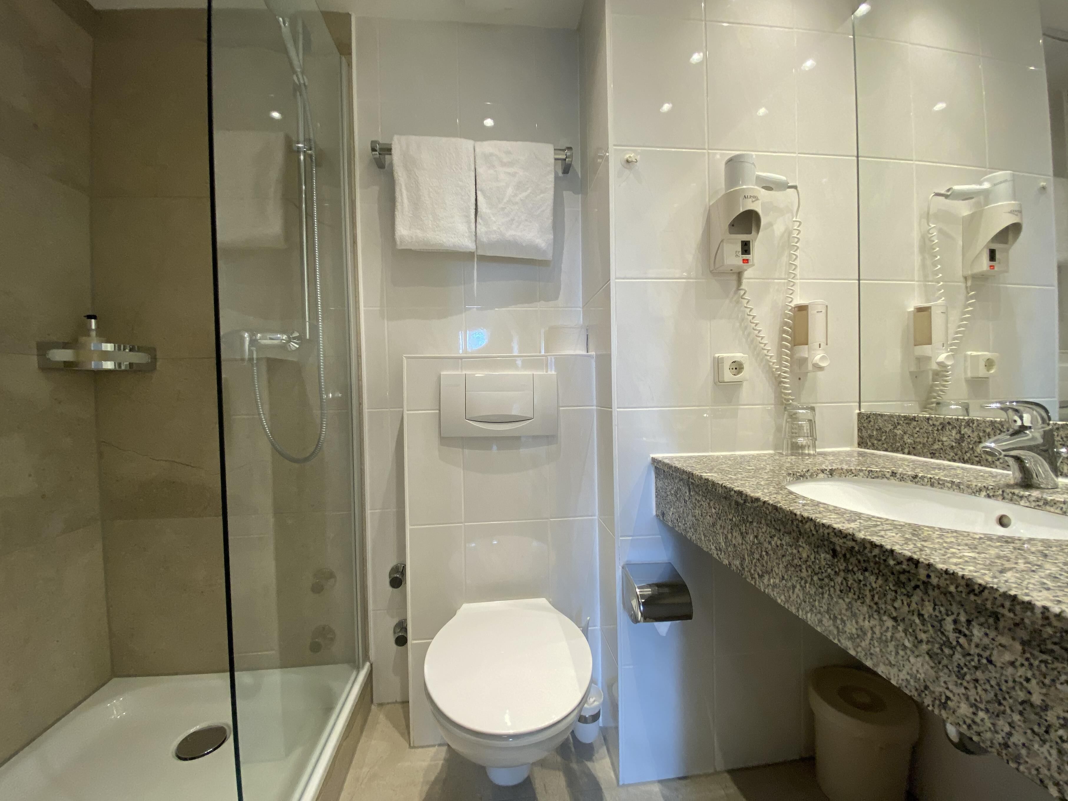 Une salle de bain moderne avec une douche à parois de verre, des toilettes blanches et un lavabo en granit avec un miroir.