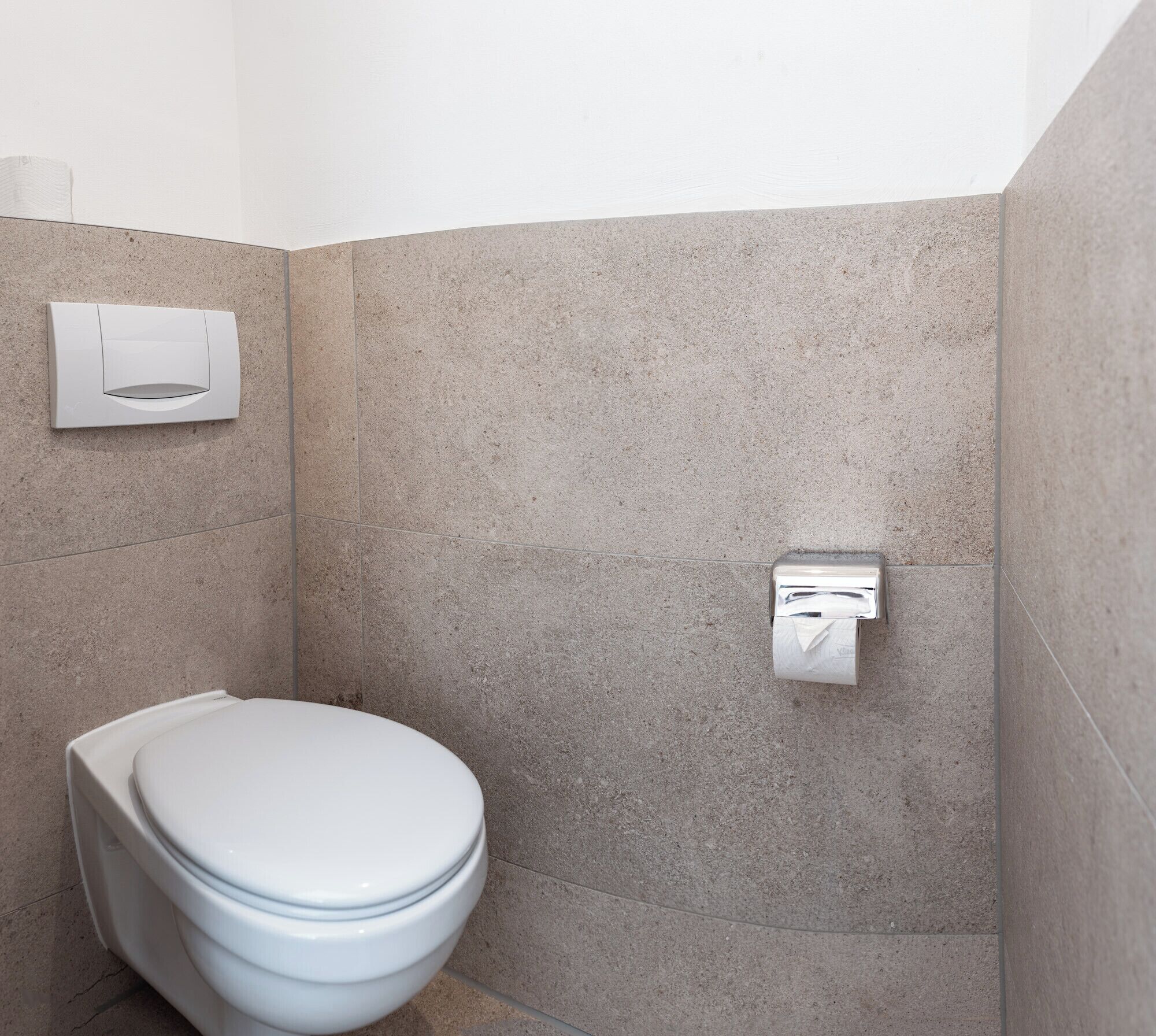 Ein modernes Badezimmer mit einer weißen Toilette, einem Papierhandtuchspender und einem an der Wand befestigten Seifenspender.