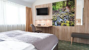 Una habitación de hotel con cama, escritorio, televisor y un amplio ventanal con cortinas.