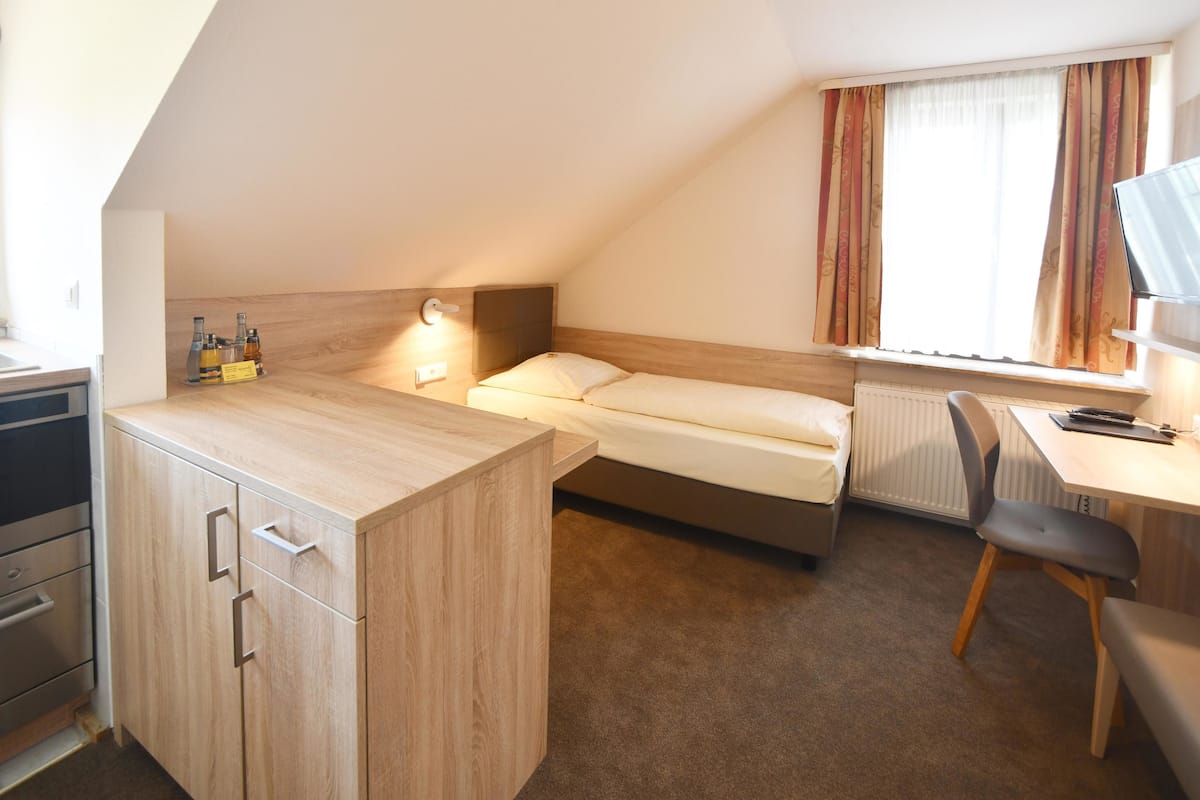 Una habitación pequeña y moderna con cama, escritorio y kitchenette.