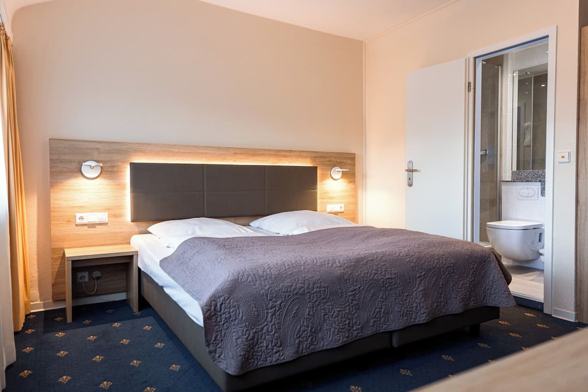 Habitación de hotel con cama, mesitas de noche y baño con inodoro y ducha.