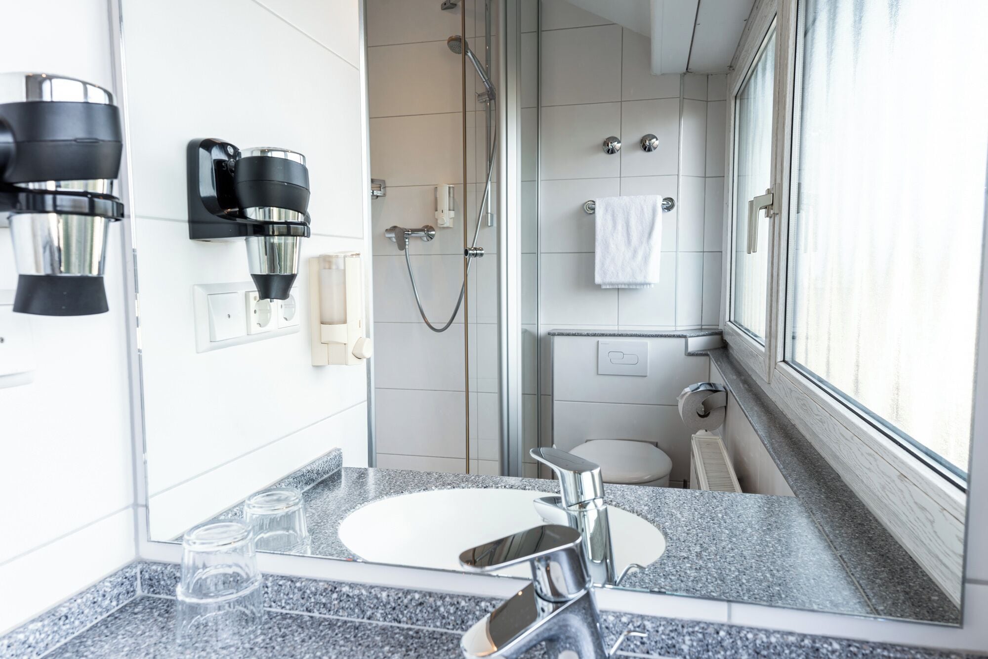 A modern bathroom with a granite countertop, a sink, a mirror, a shower, and a toilet.