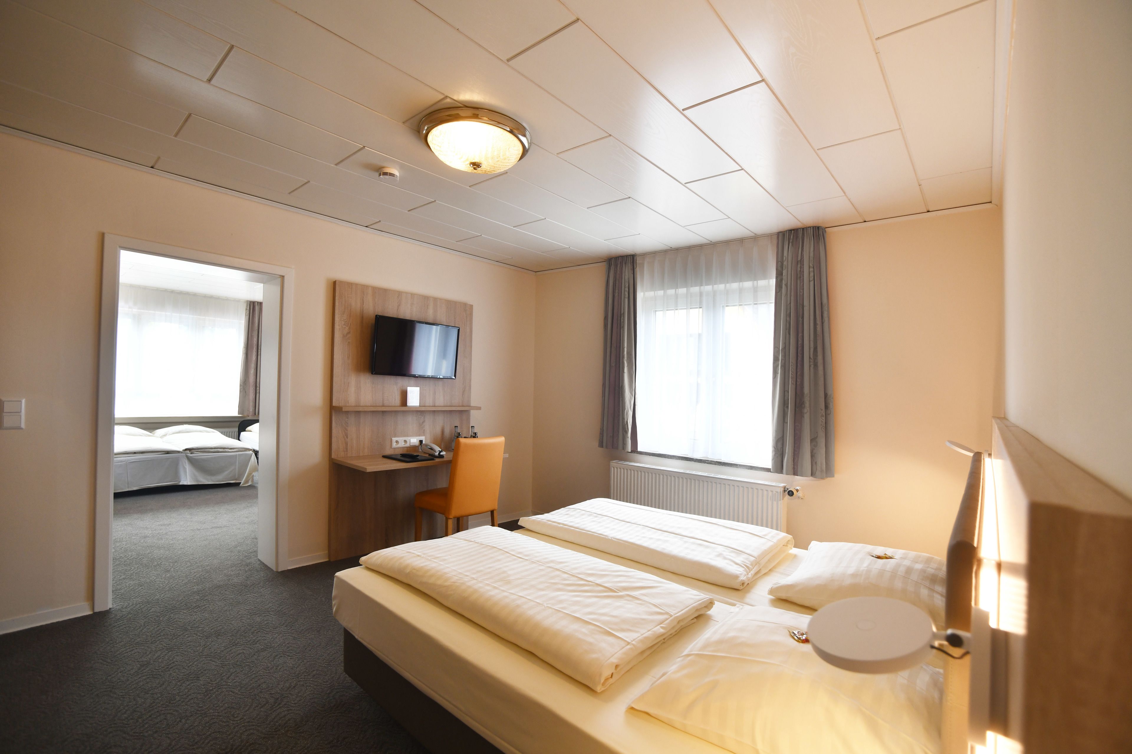 A hotel room with two beds, a desk, a chair, a television, and a window with curtains.