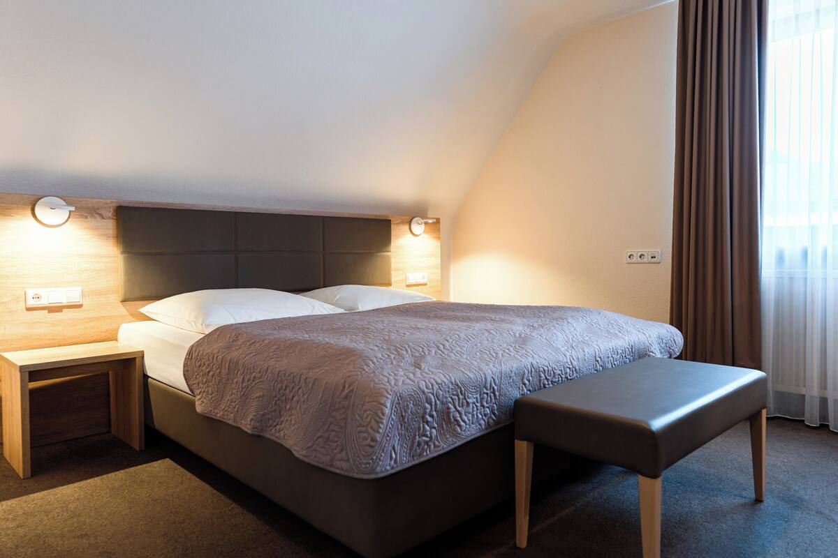 Una habitación de hotel moderna con una cama grande, mesitas de noche, un banco y vistas al exterior.