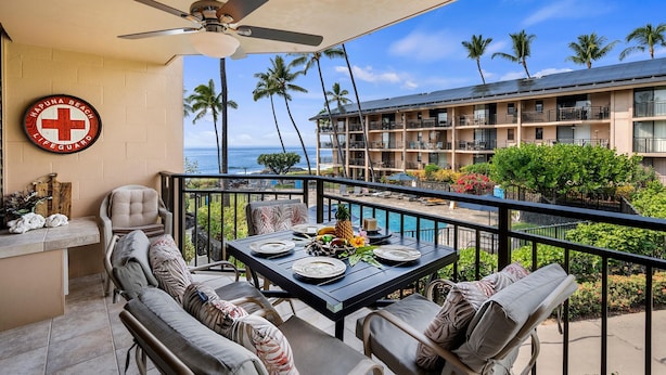 Ein Balkon mit Esstisch, einem Rettungsschwimmer-Schild und Blick auf das Meer und Palmen.
