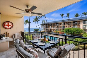 Een balkon met een eettafel, een bord met daarop een afbeelding van een strandwacht en uitzicht op de oceaan en palmbomen.
