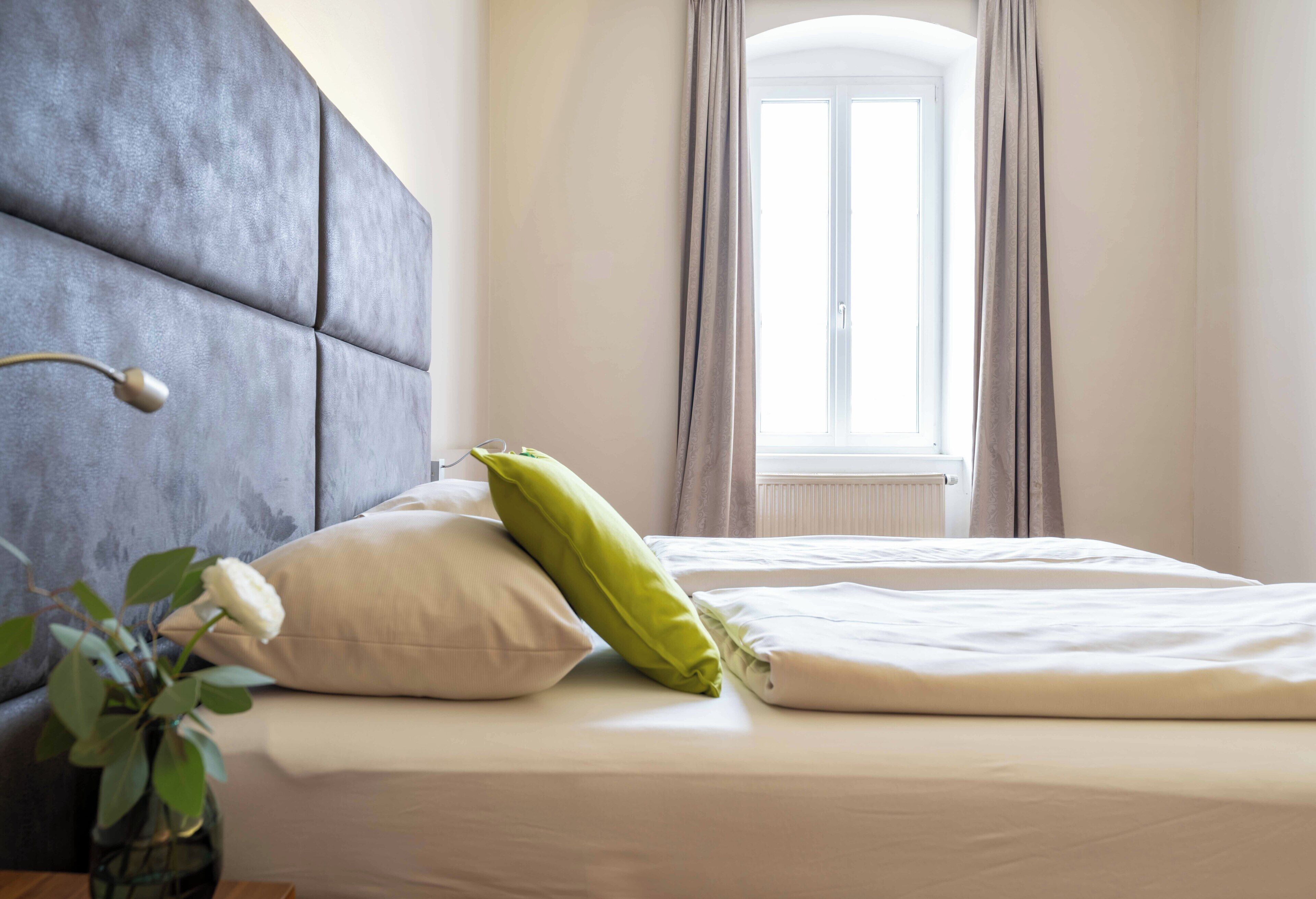 A neatly made bed with pillows, a bedside lamp, and a window with curtains.