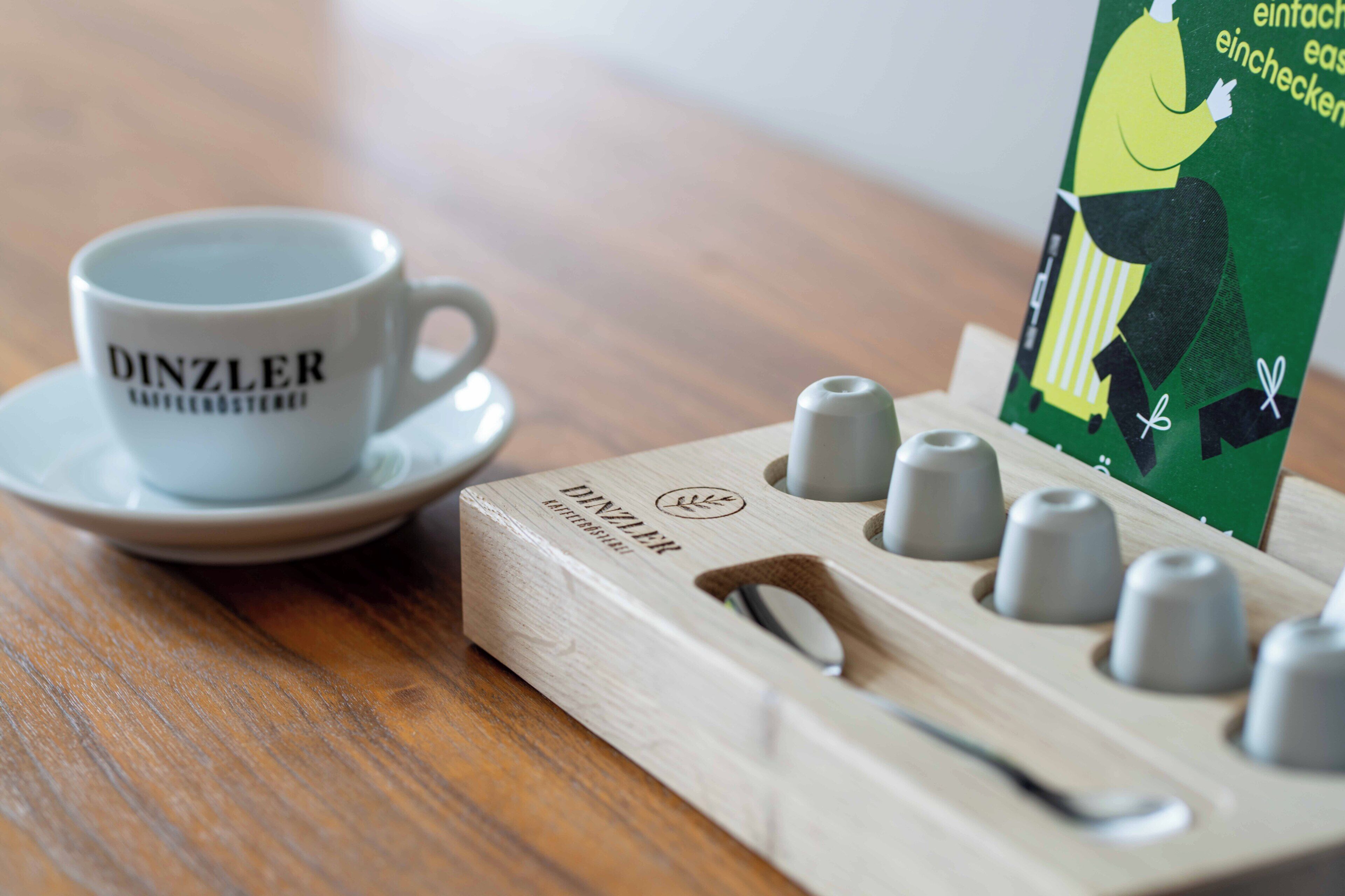 A wooden coffee machine with a cup and saucer labeled "DINZLER" on a wooden table.