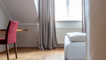 A room with a bed, a chair, a window with curtains, and a radiator.