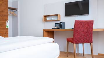 Una habitación de hotel con cama, escritorio con silla, televisor y cafetera.