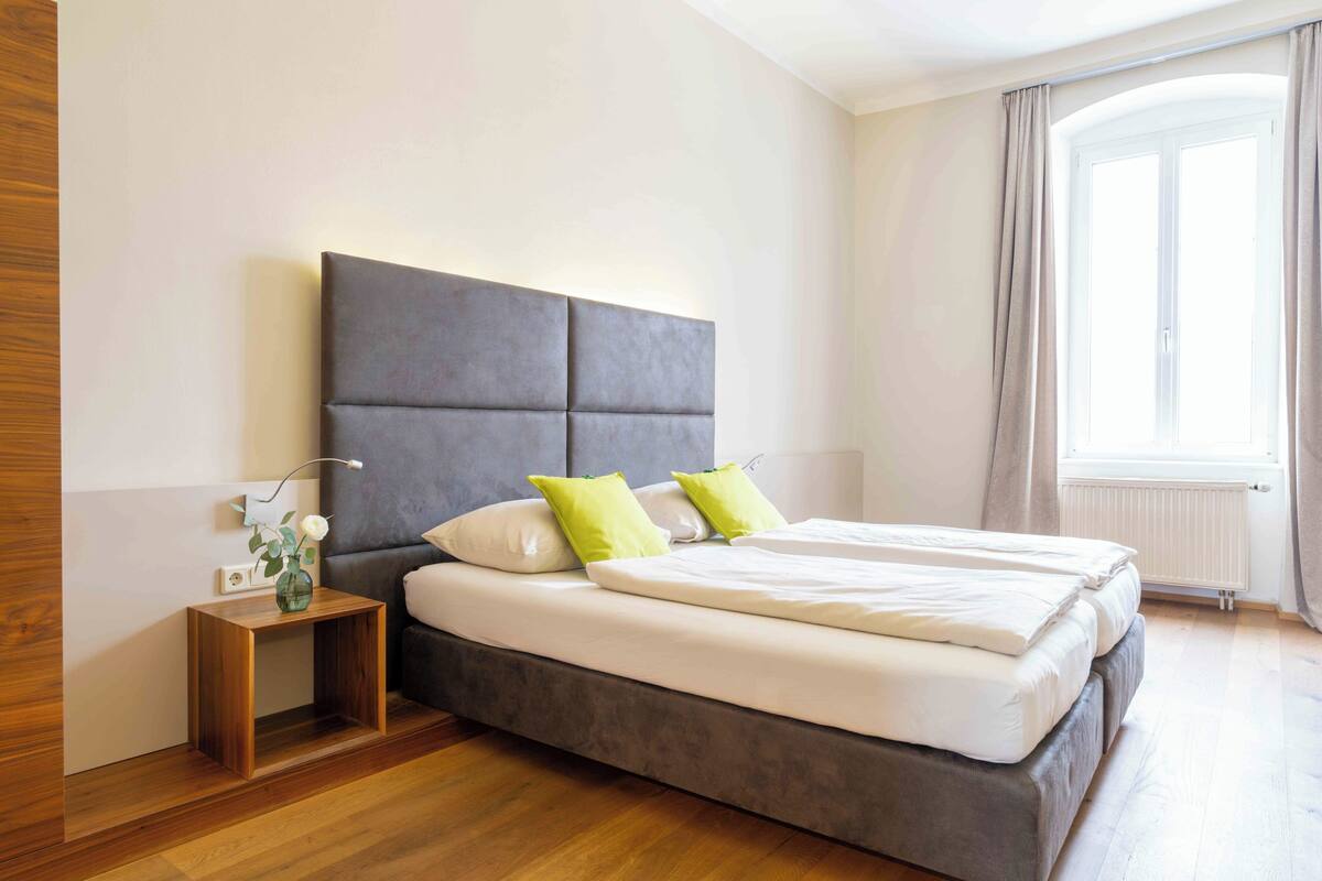 Une chambre moderne avec un grand lit, une table de chevet et une fenêtre avec des rideaux.