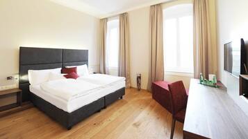 Habitación de hotel con cama, mesita de noche, silla, escritorio, televisor y ventanas amplias.