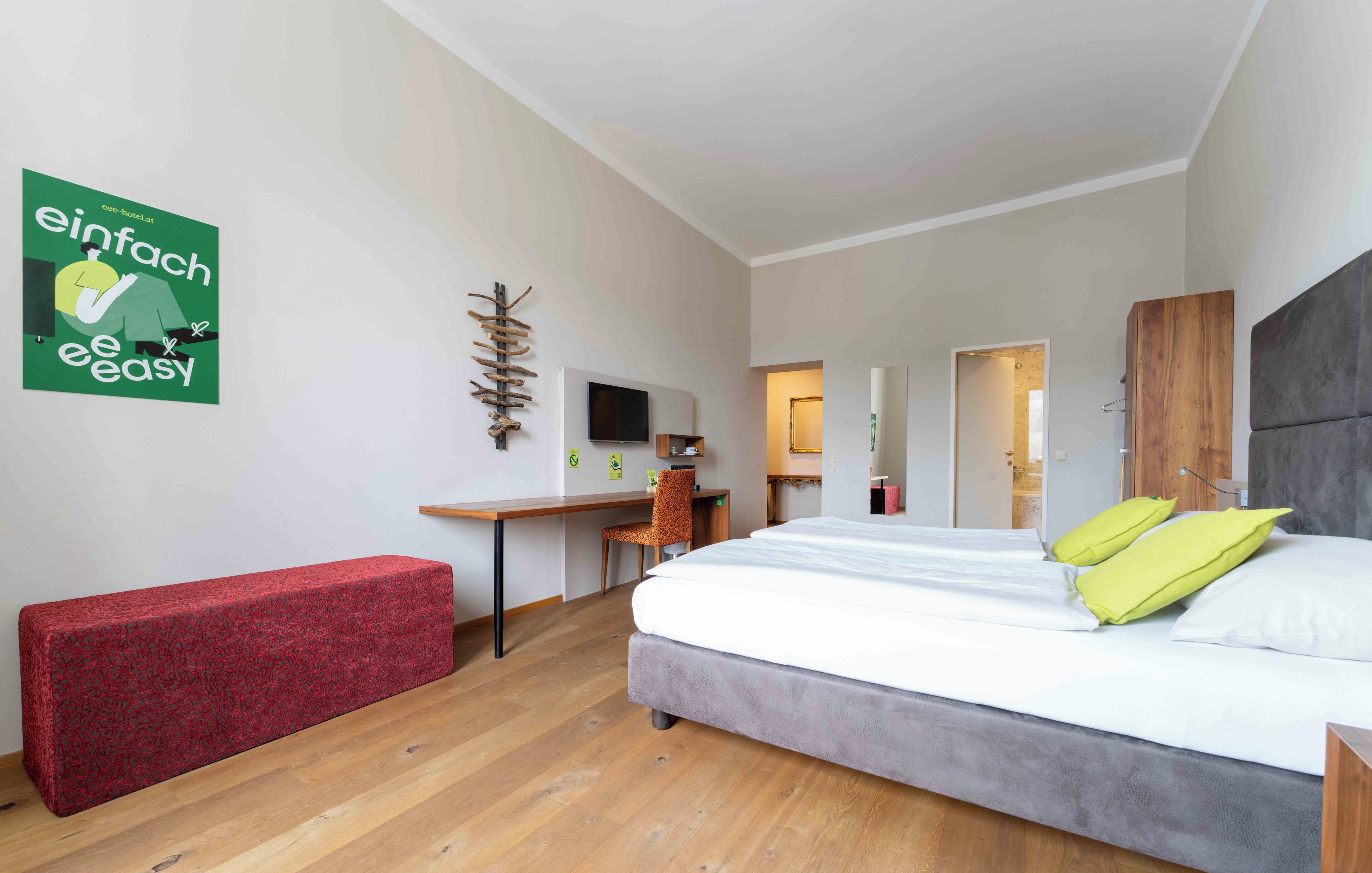 Ein modernes Hotelzimmer mit einem großen Bett, einem Schreibtisch, einem Sessel und einer roten Bank.