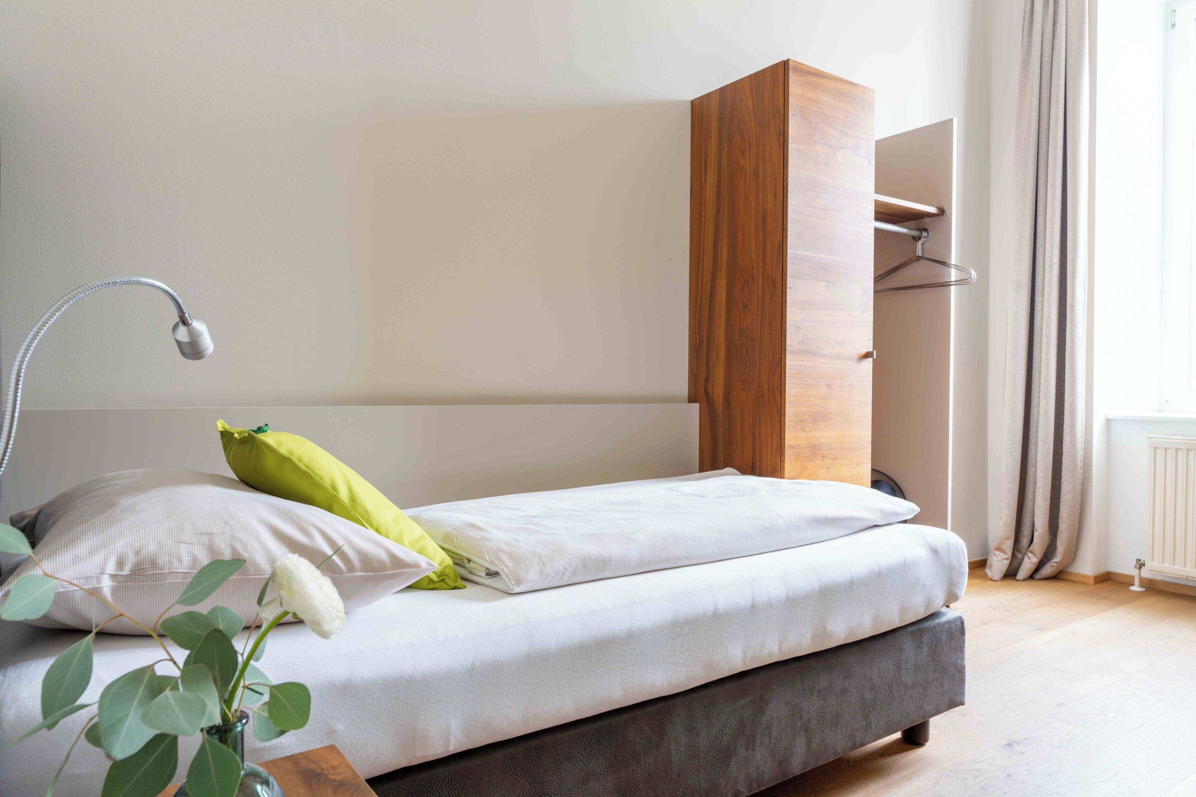 Ein modernes Schlafzimmer mit Bett, Nachttischlampe, Kleiderhaken und einem Fenster mit Vorhängen.