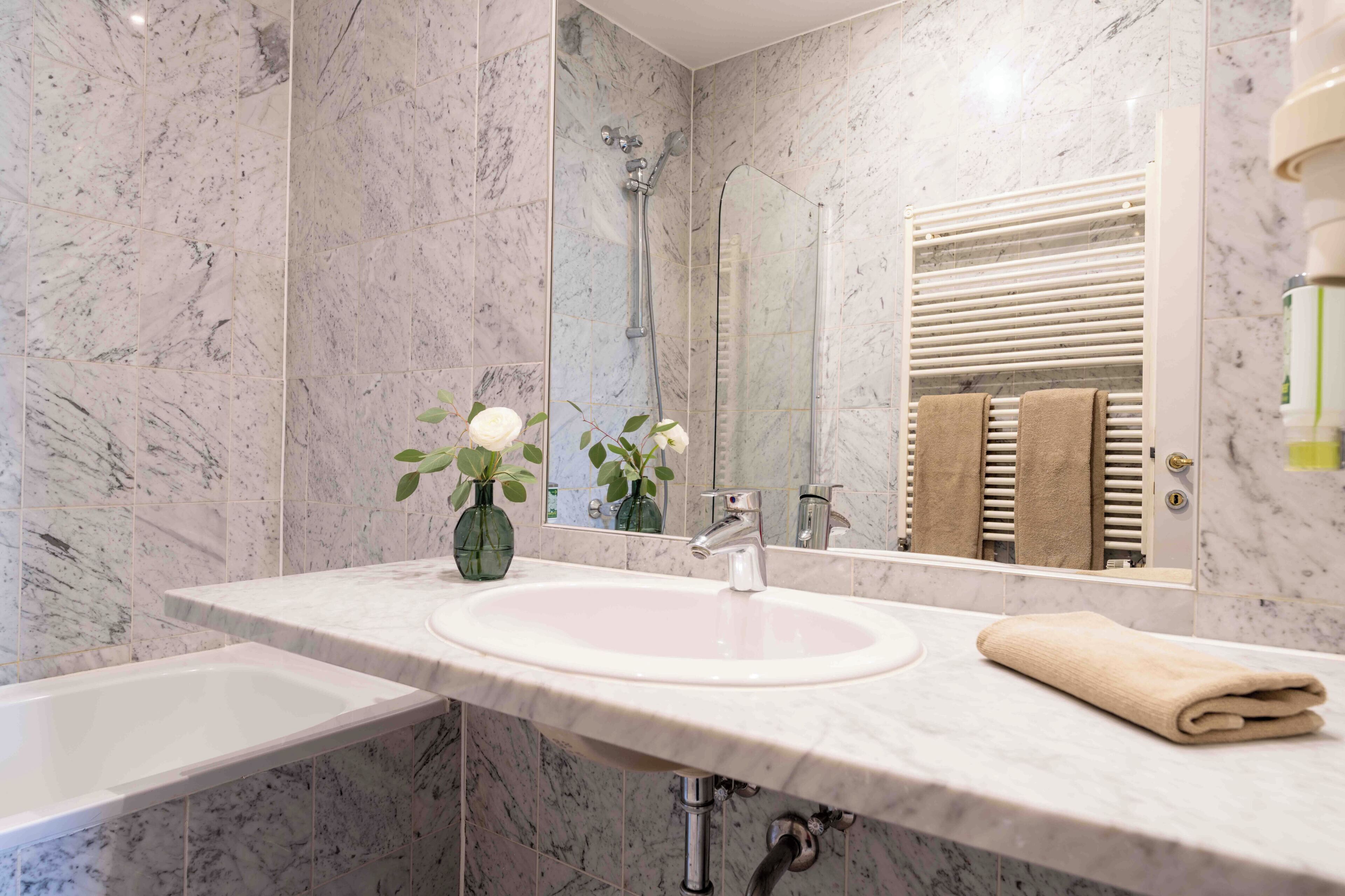 Een badkamer met een marmeren wastafel, een spiegel, een douche en een handdoekrek.