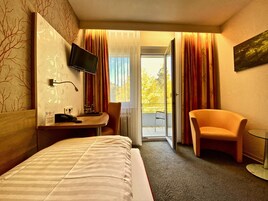 Hotellihuone, jossa on s änky, työpöytä tuolilla, televisio ja parveke, jossa on verhot.