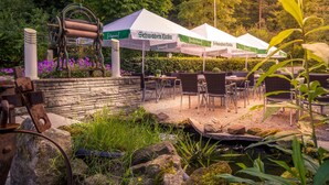 A garden setting with outdoor seating under tents, a rustic metal structure, and a small water feature. - Hotel Kulinarium an der Glems (Stuttgart)