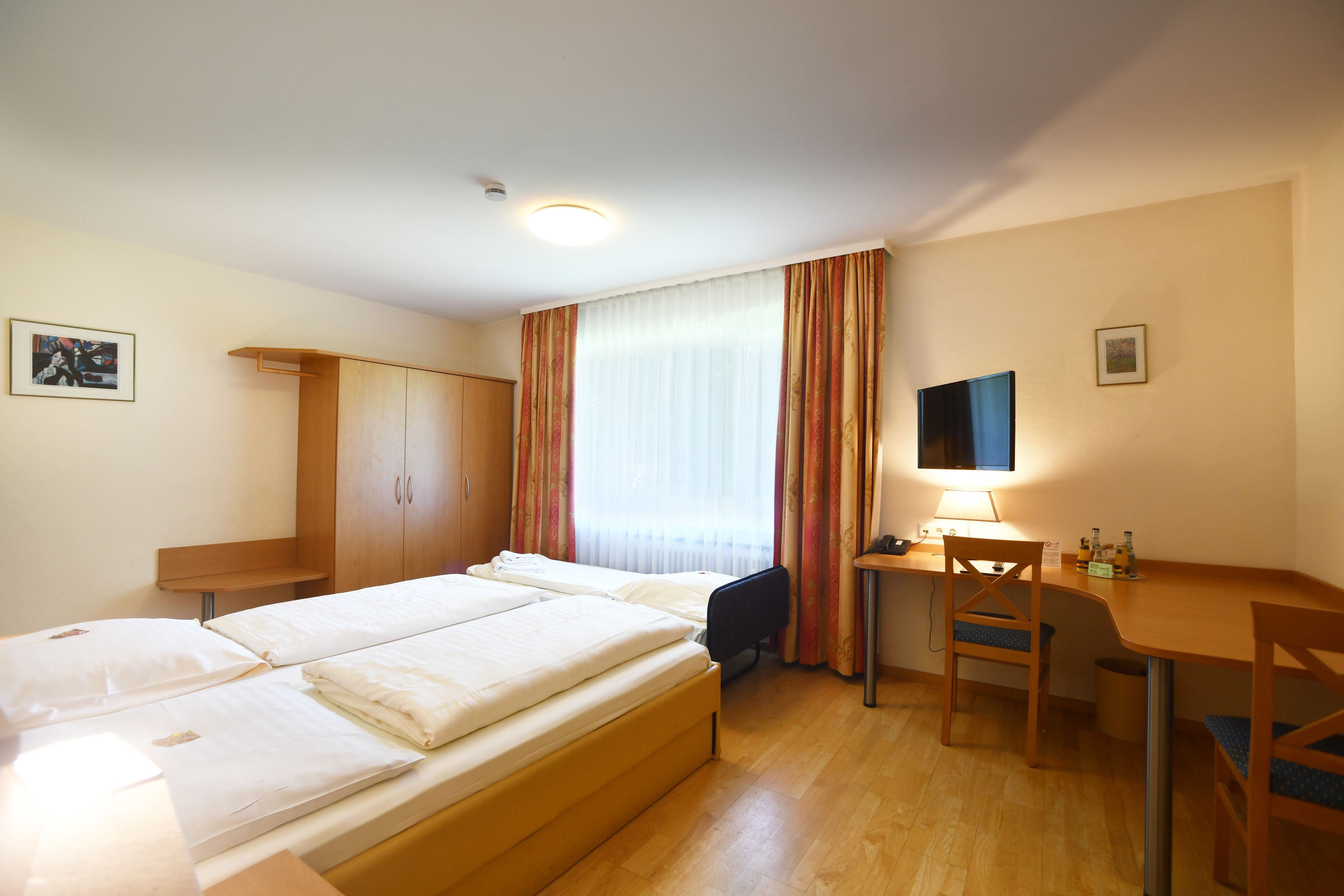 Ein Hotelzimmer mit einem Bett, einem Schreibtisch, einem Stuhl, einem Fernseher und einem Kleiderschrank.