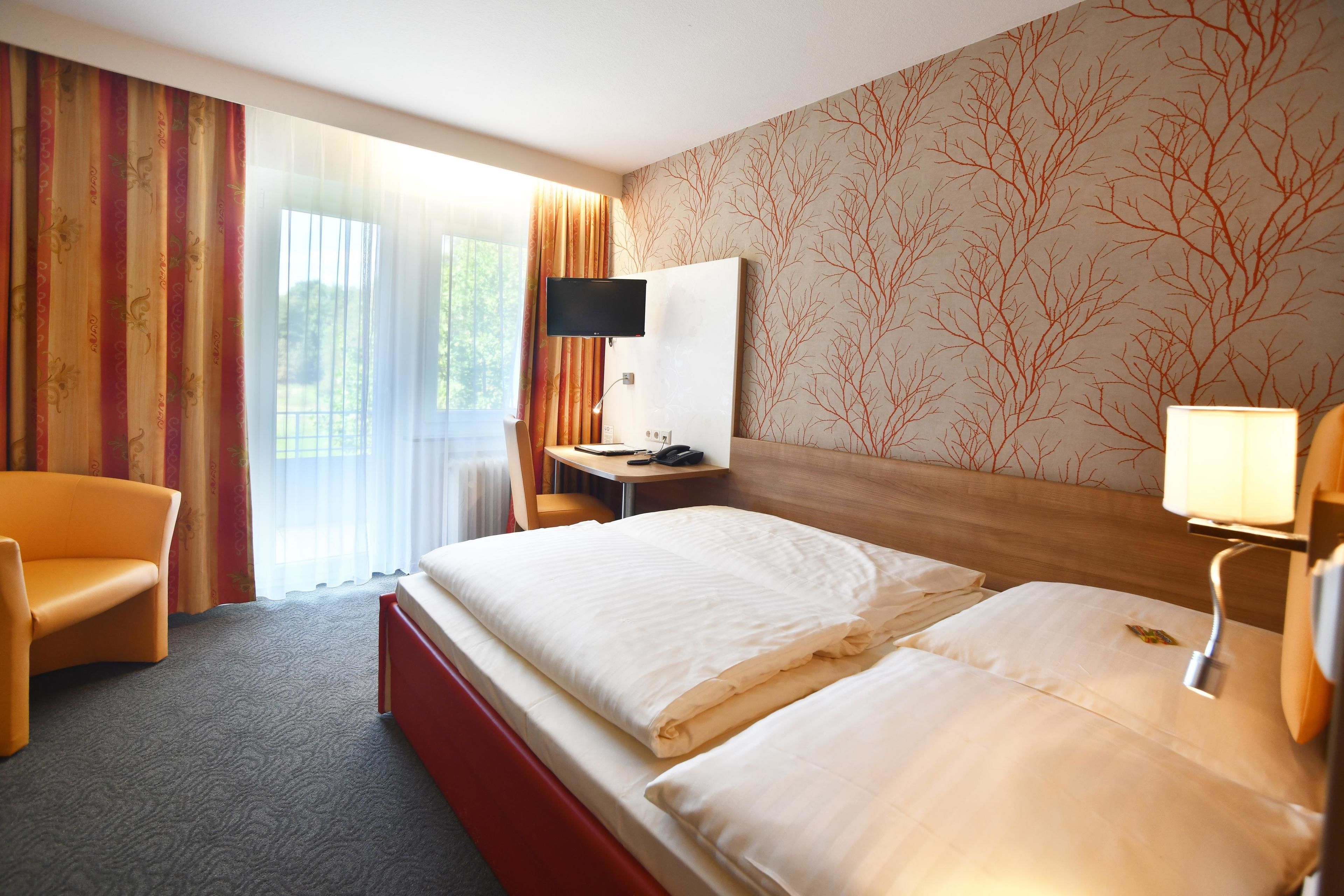 Een hotelkamer met een groot bed, een bureau met een televisie, een stoel en een raam met gordijnen.