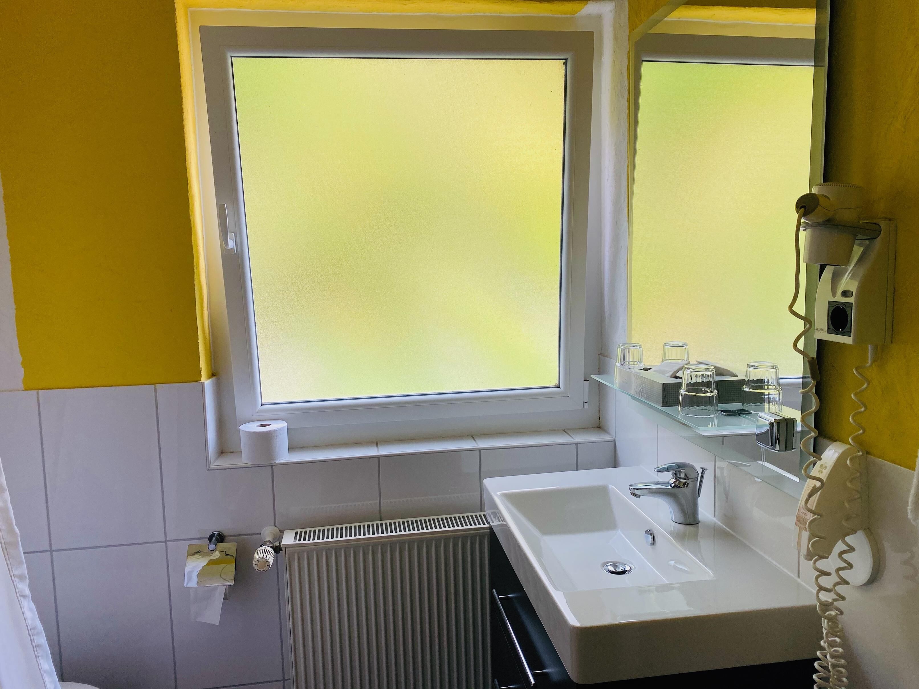 A bathroom with a window, a sink, a mirror, and a radiator.
