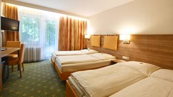 Habitació d'hotel amb dos llits individuals, un escriptori amb cadira, televisió i finestra amb cortines.