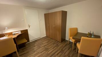 Una habitación con suelo de madera, un escritorio con lámpara, un armario y una mesa de comedor con sillas.