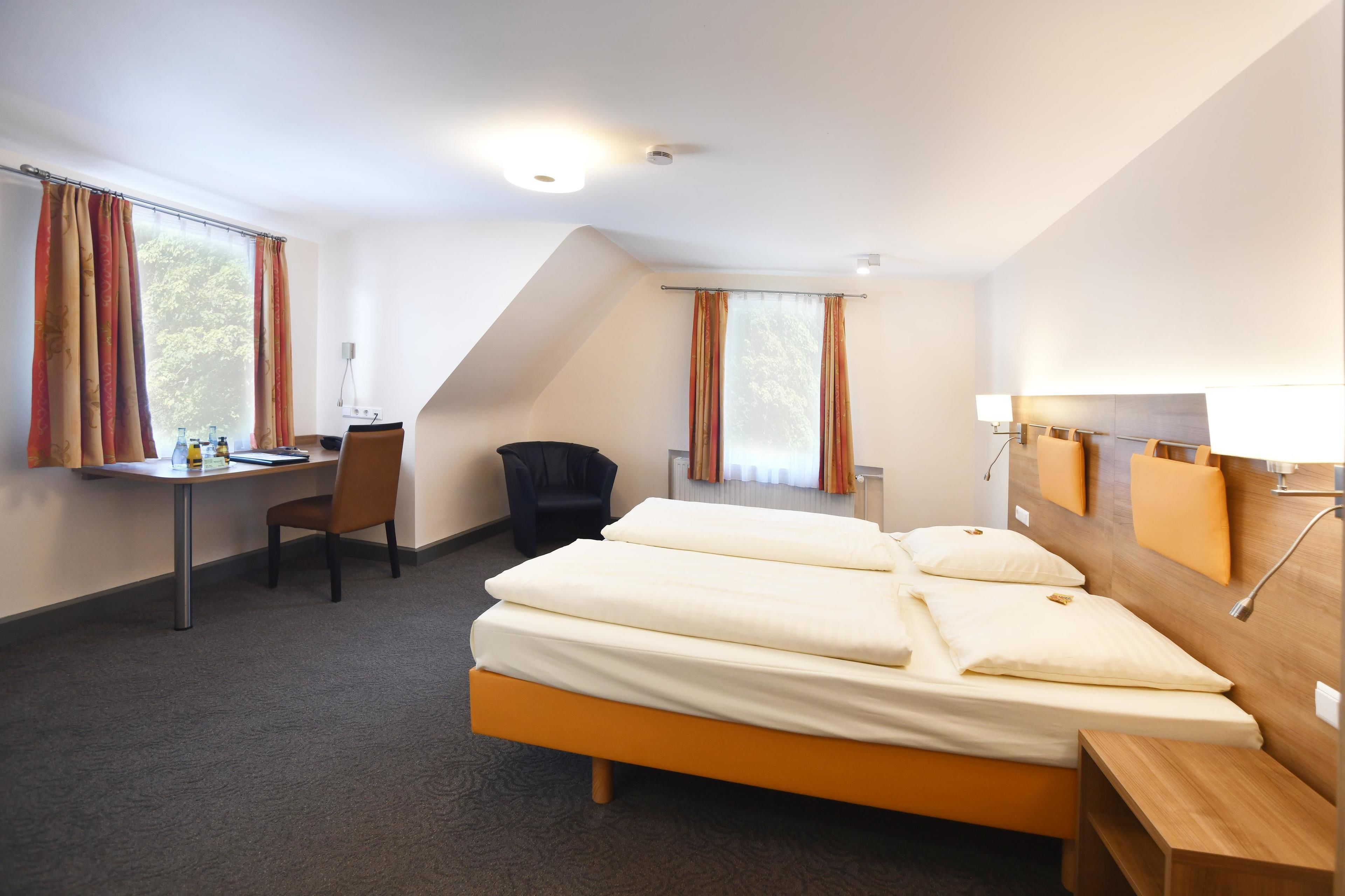A hotel room with a bed, desk, chair, and windows.