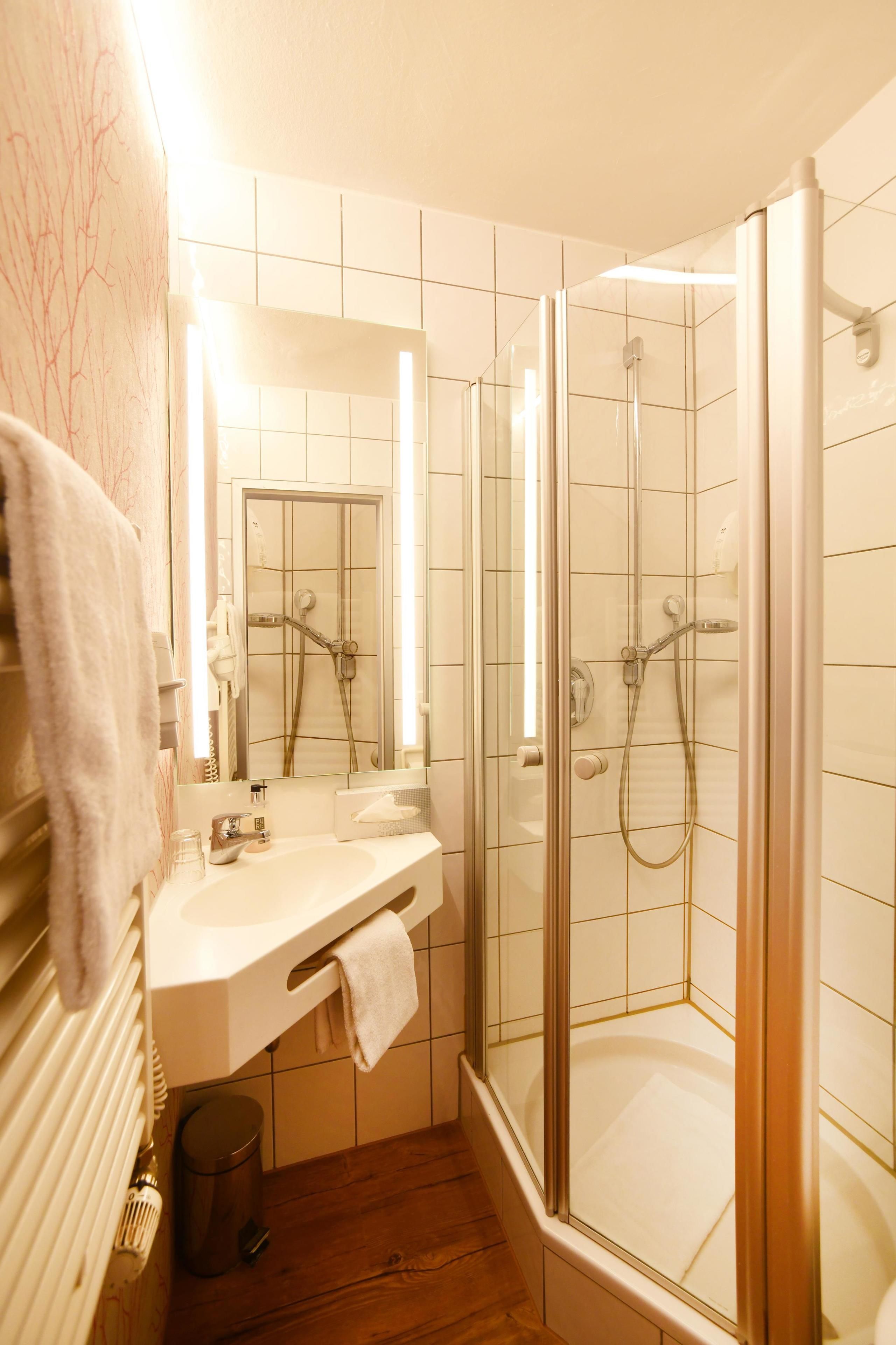 Un baño con ducha de vidrio, lavabo con espejo y suelo de madera.