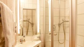 Un baño con ducha de vidrio, lavabo con espejo y suelo de madera.