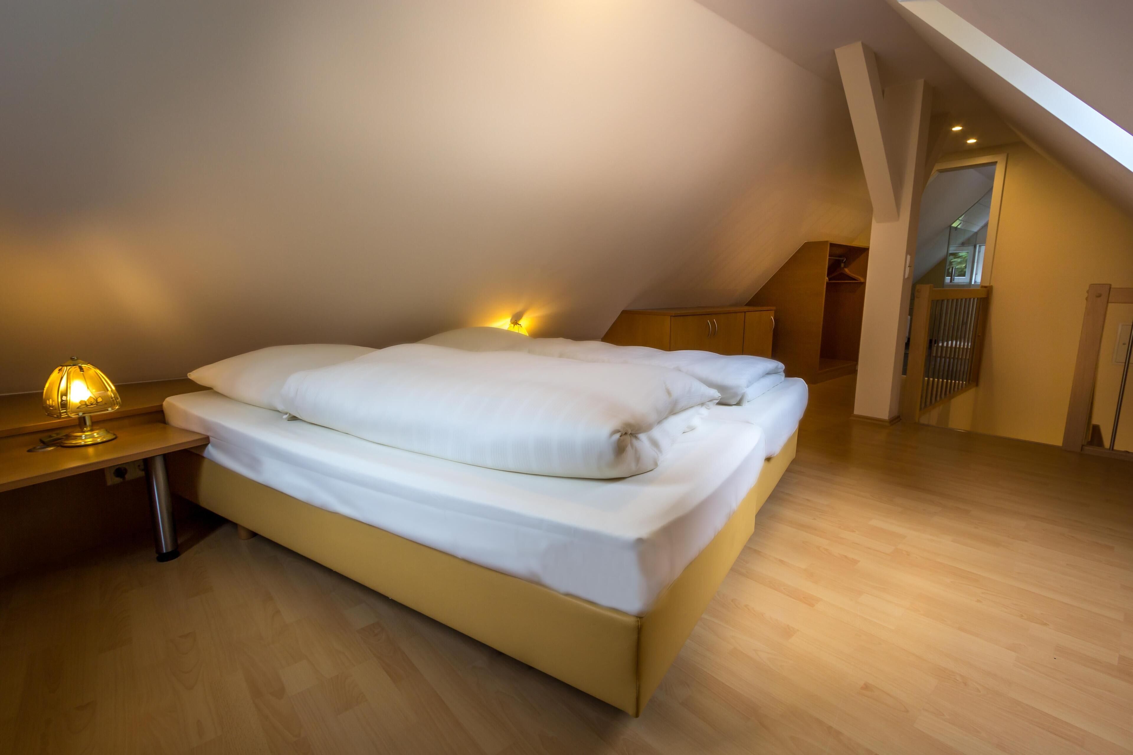 Een slaapkamer met een bed, een bedlamp en een houten vloer.