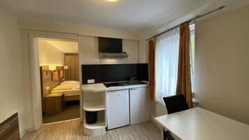 A compact hotel room with a kitchenette, a bed, a desk, and a chair.