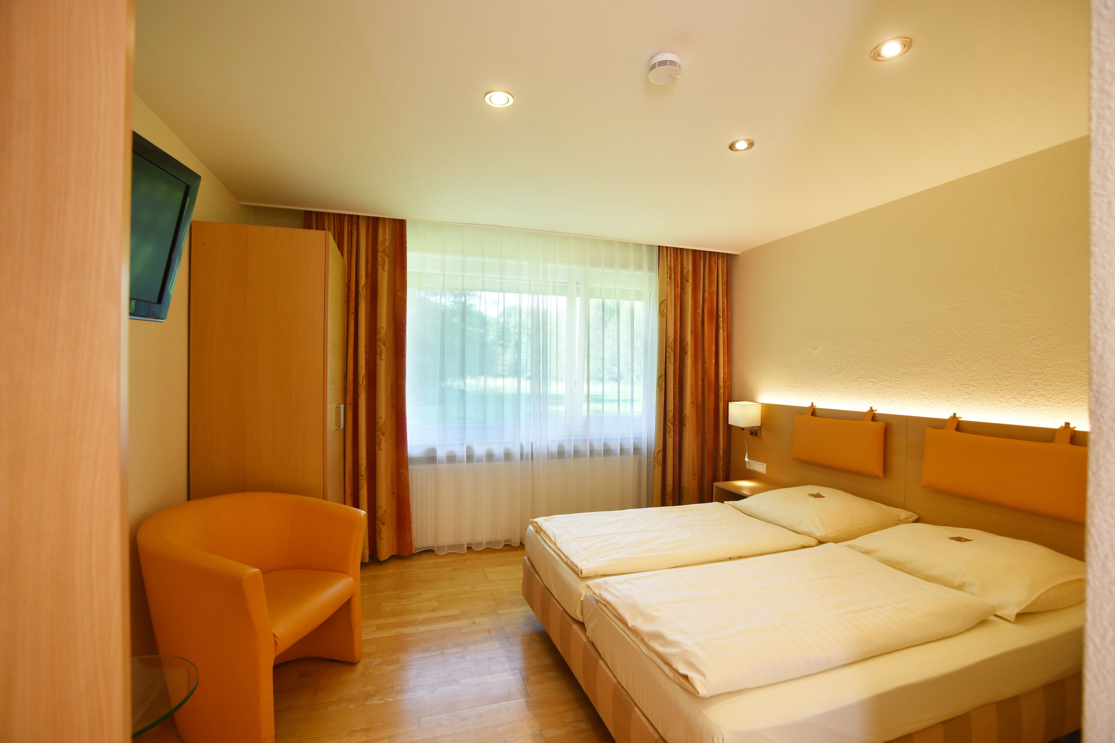 A hotel room with a bed, a chair, and a television on the wall.