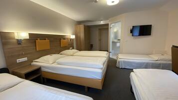 Een hotelkamer met drie eenpersoonsbedden, een houten hoofdbord, nachtlampjes, een flatscreen televisie en een deur naar een badkamer.