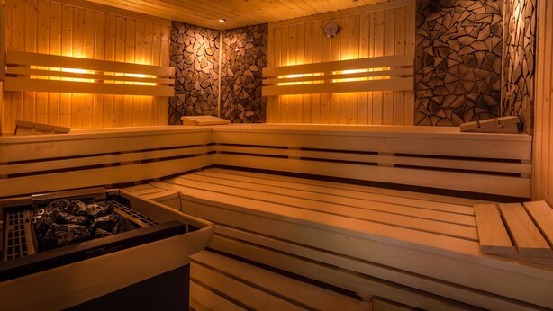 A sauna with wooden benches and a stone wall. - Hotel Kulinarium an der Glems (Stuttgart)