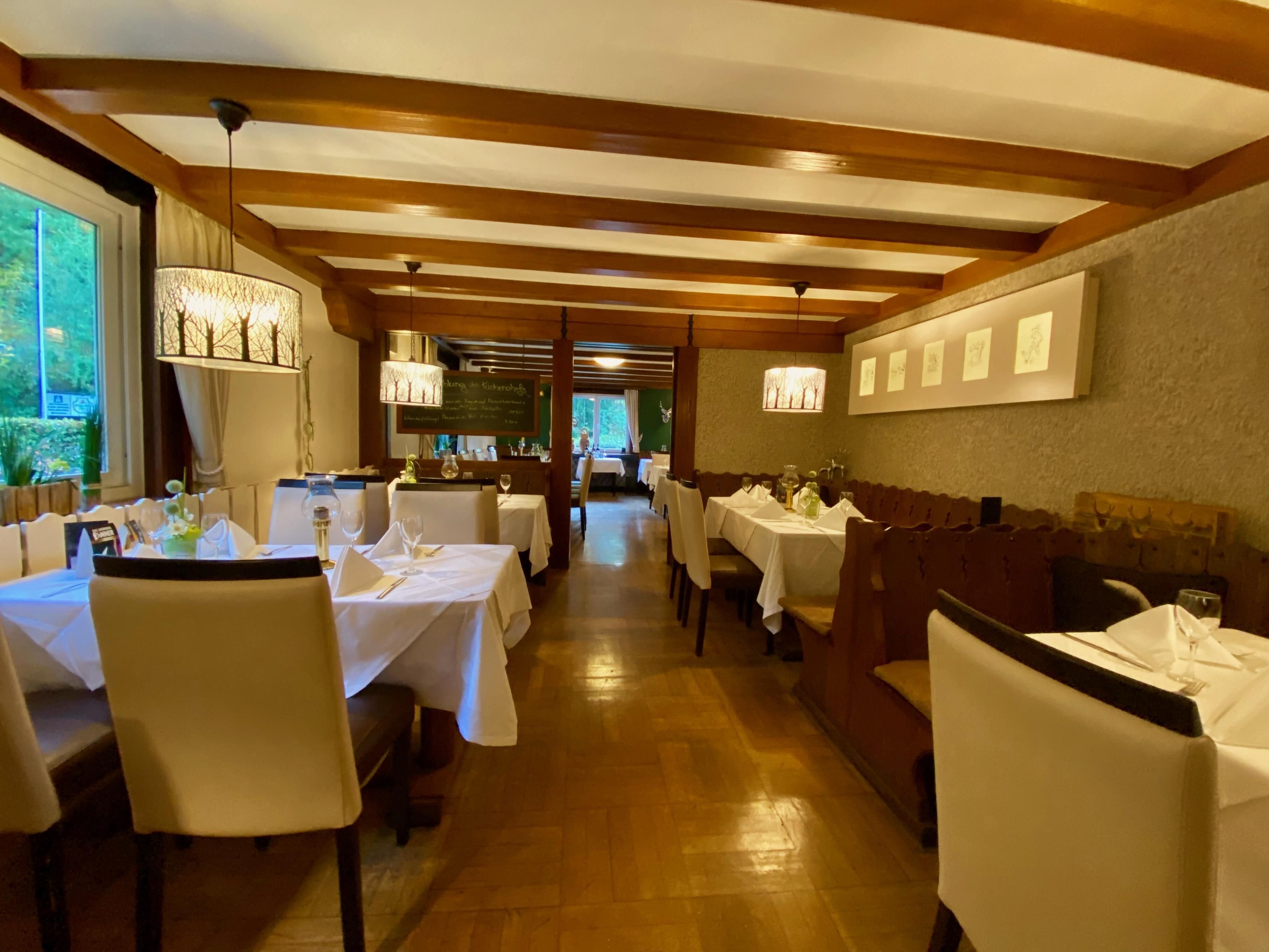 Een restaurant met houten balken in het plafond, witte tafellakens en stoelen.