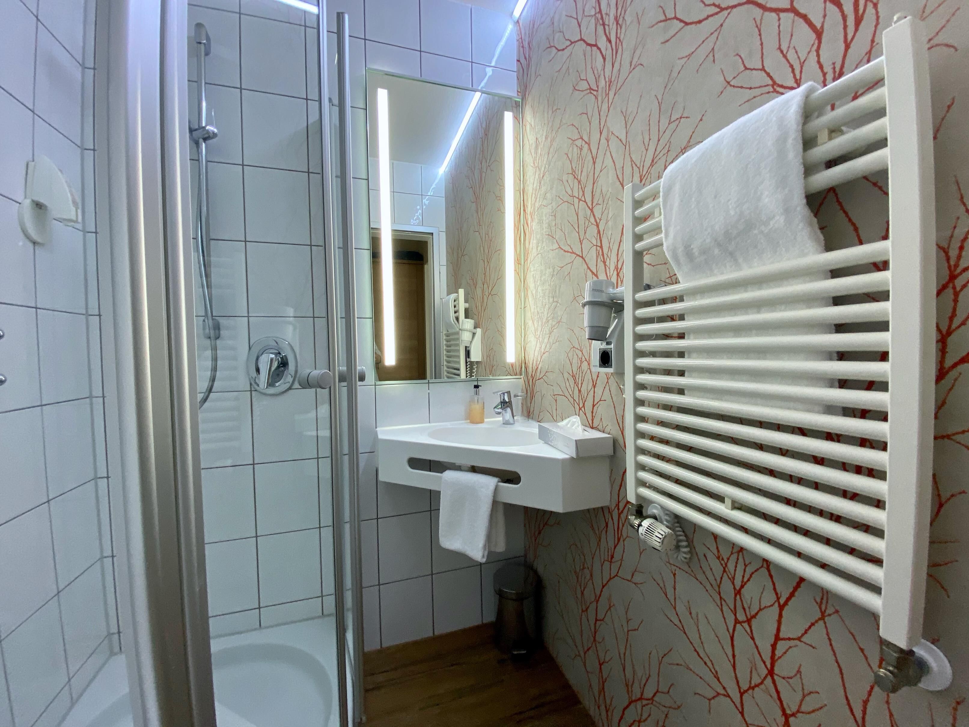 A modern bathroom with a glass-enclosed shower, a white sink, and a towel rack.