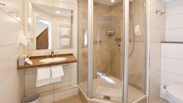 Un baño moderno con ducha de vidrio, lavamanos con espejo e inodoro.