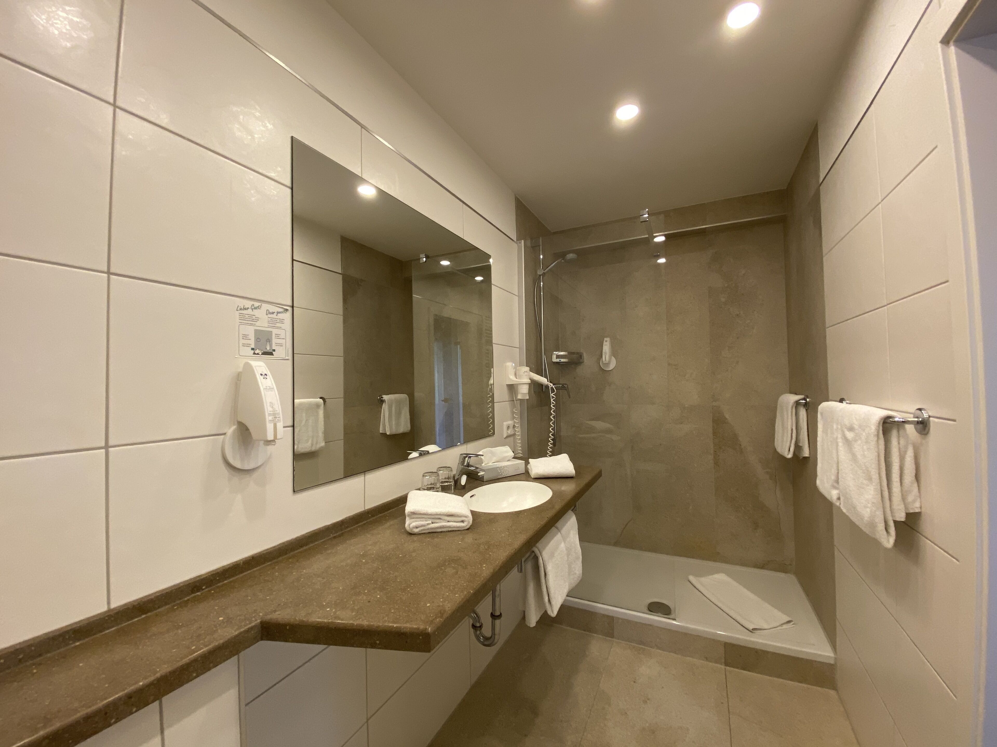 Un baño moderno con un espejo grande, un lavamanos, una ducha y un perchero para toallas.