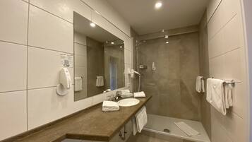 Un baño moderno con un espejo grande, un lavamanos, una ducha y un perchero para toallas.