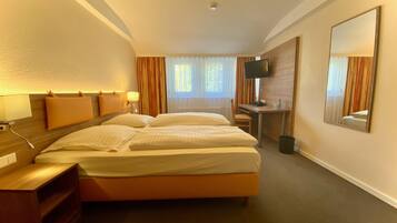Habitación de hotel con cama doble, escritorio, silla, televisor y espejo.