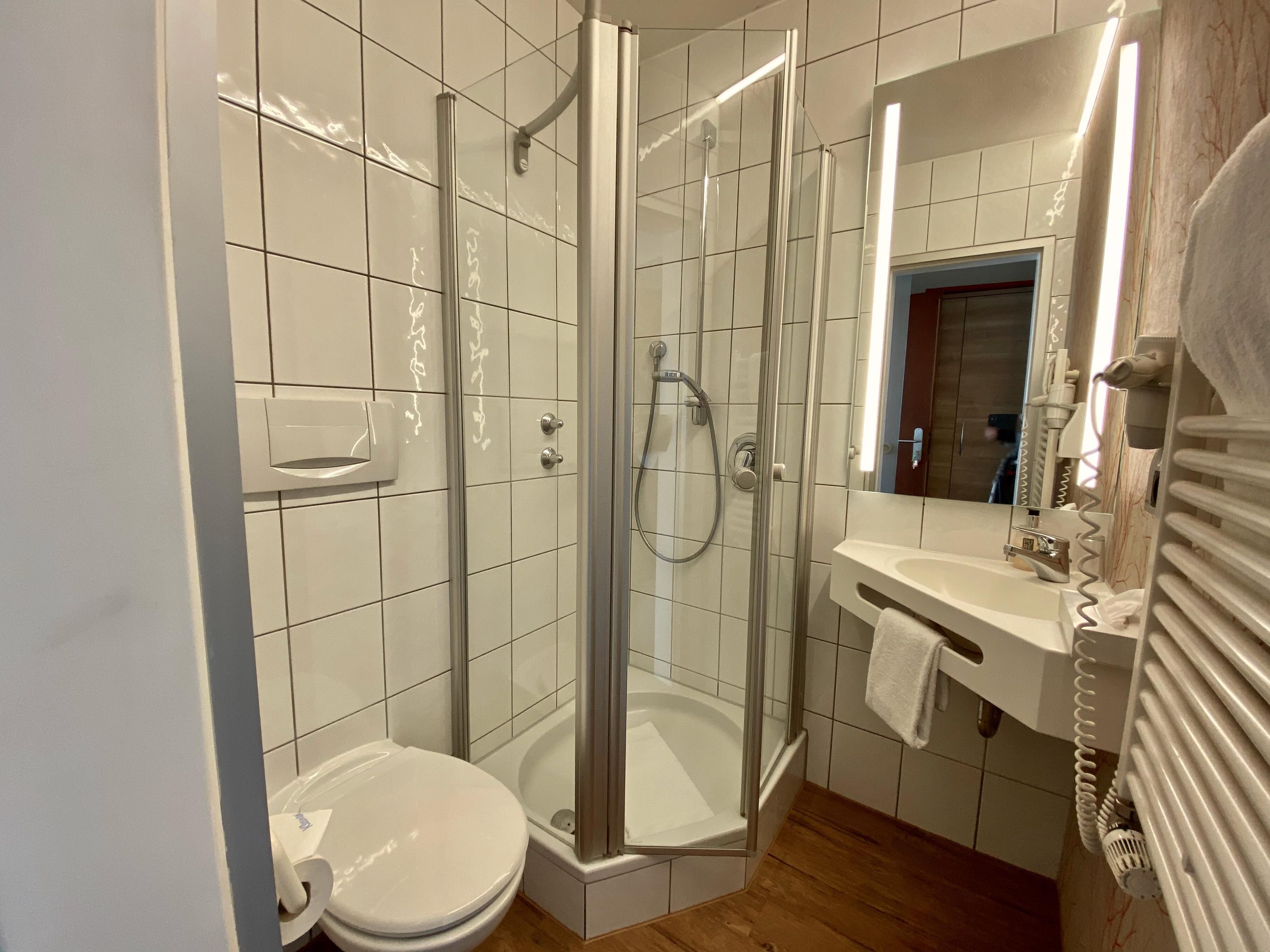 A modern bathroom with a glass-enclosed shower, a white toilet, and a sink with a towel rack.