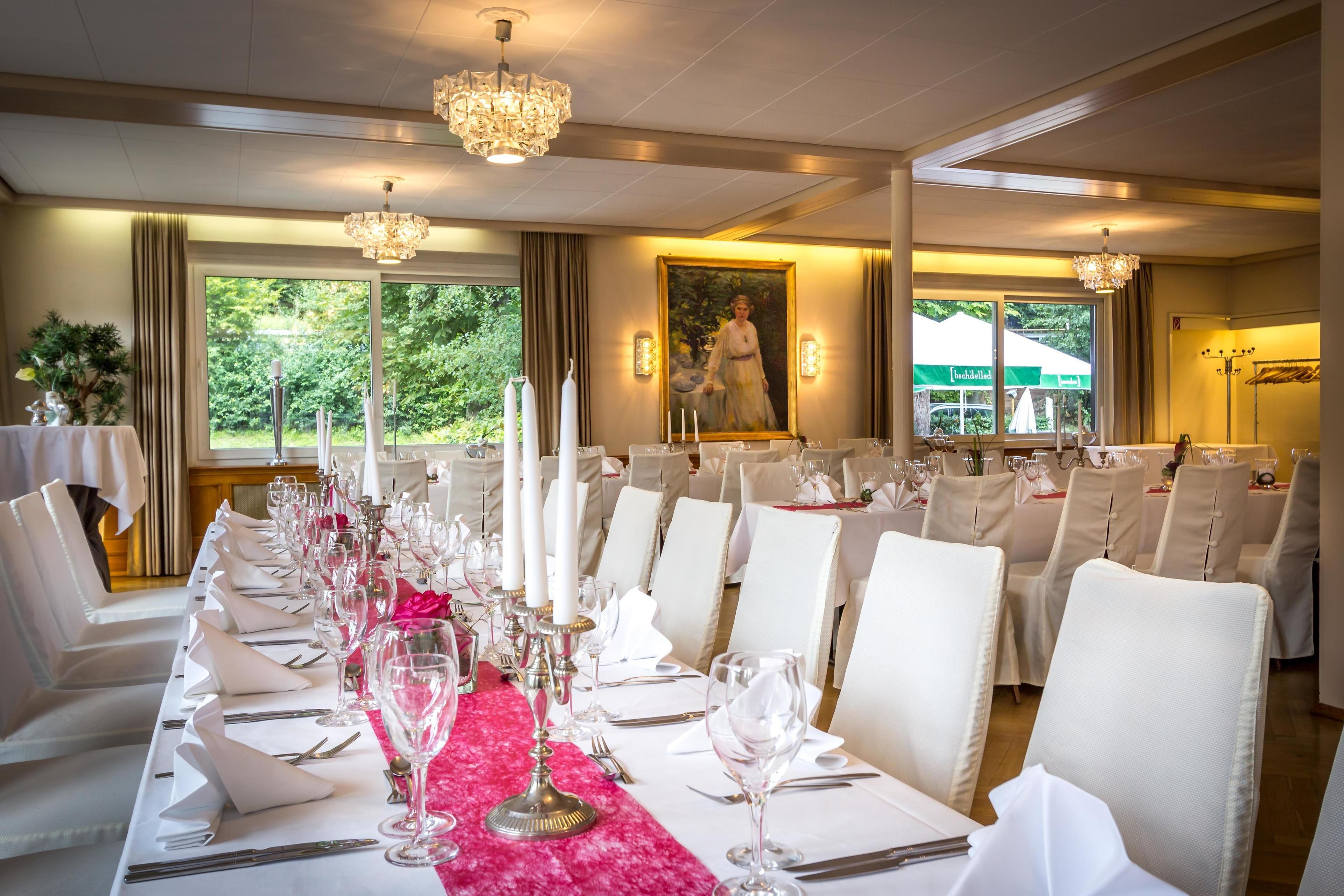 A formal dining room with a long table set for a meal, chandeliers, and a painting on the wall.