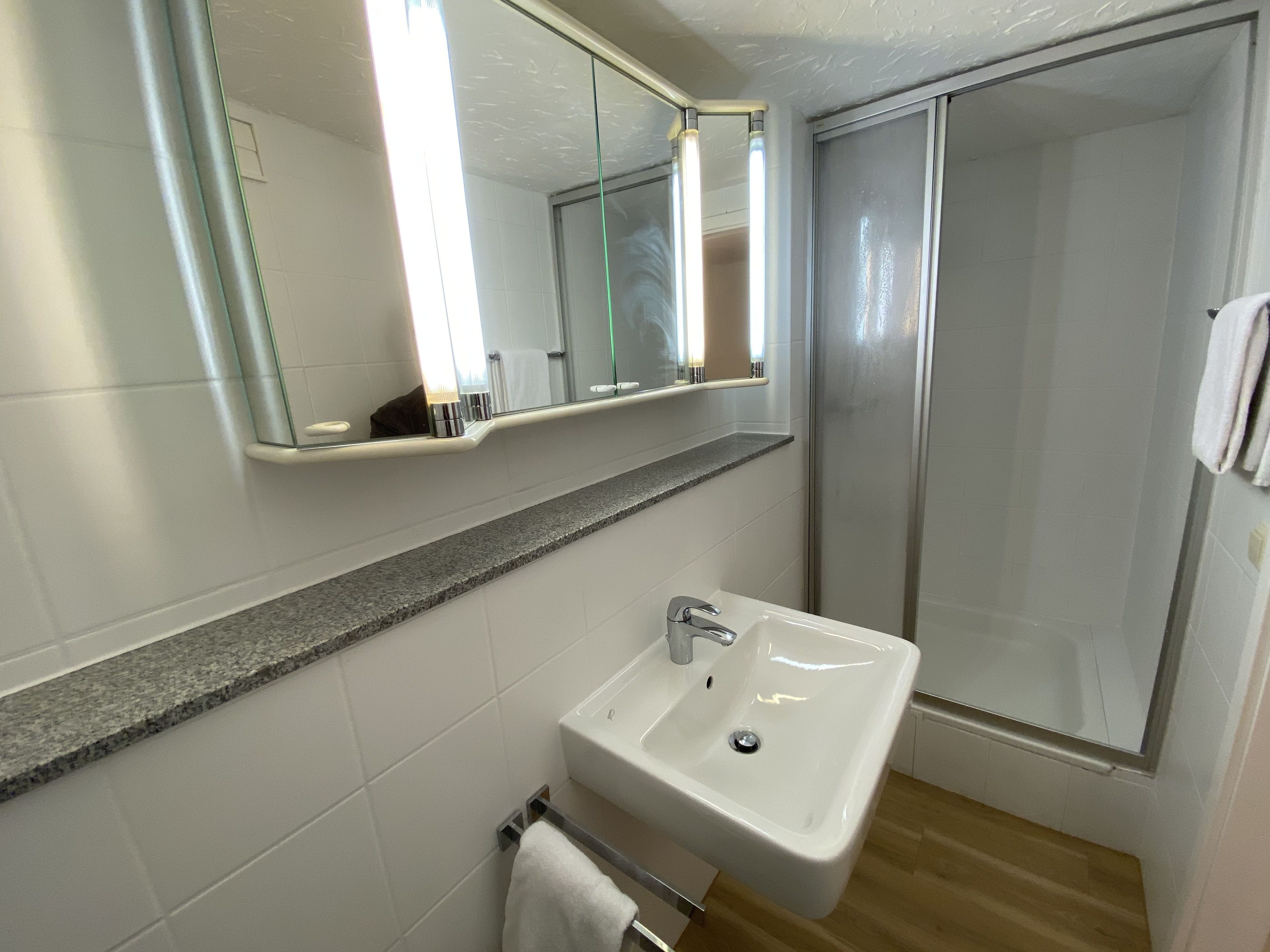 A bathroom with a white sink, a mirror, and a shower enclosure.