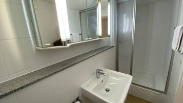 A bathroom with a white sink, a mirror, and a shower enclosure.