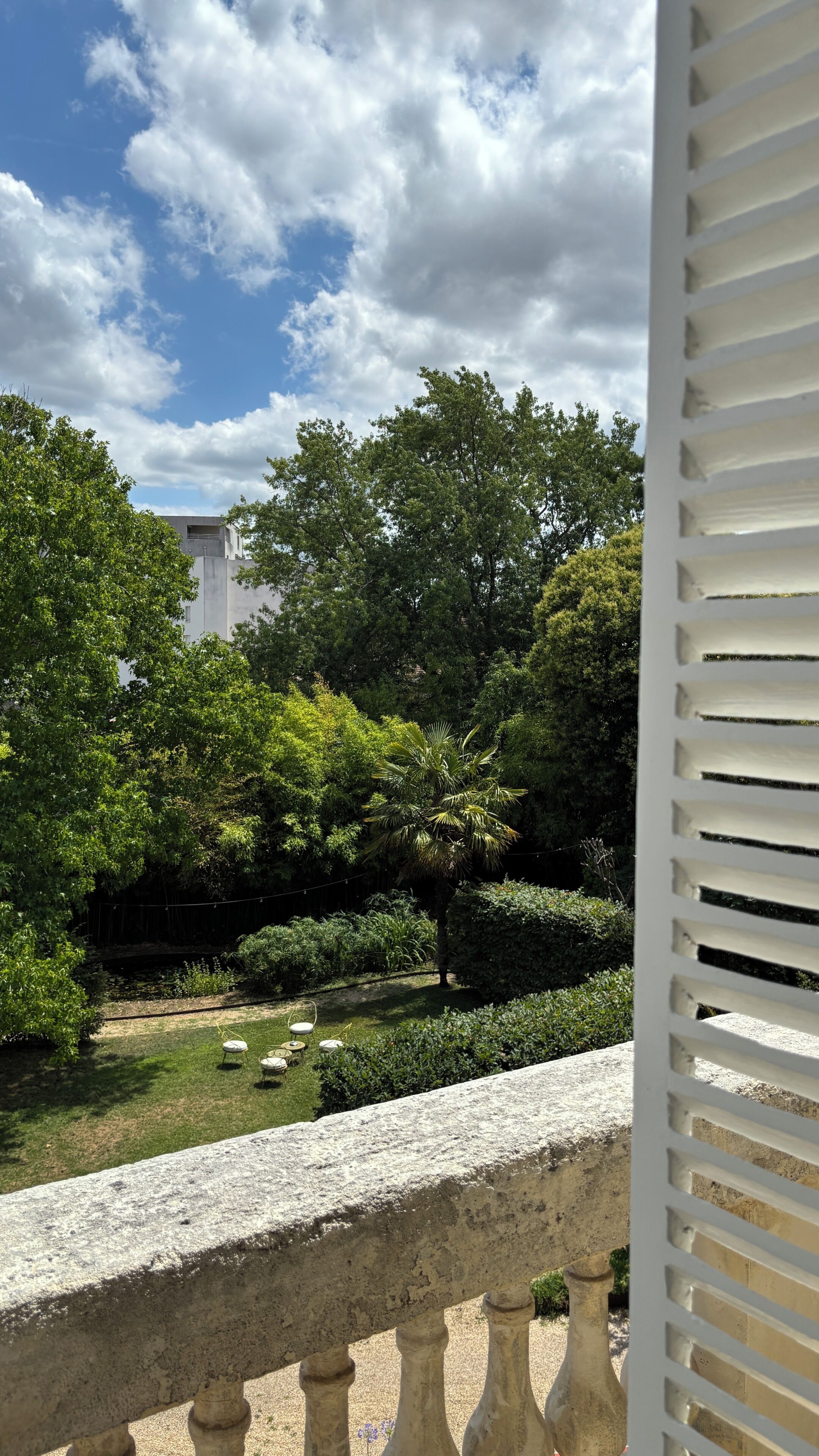 A garden with a stone balustrade, lush greenery, and a building in the background.