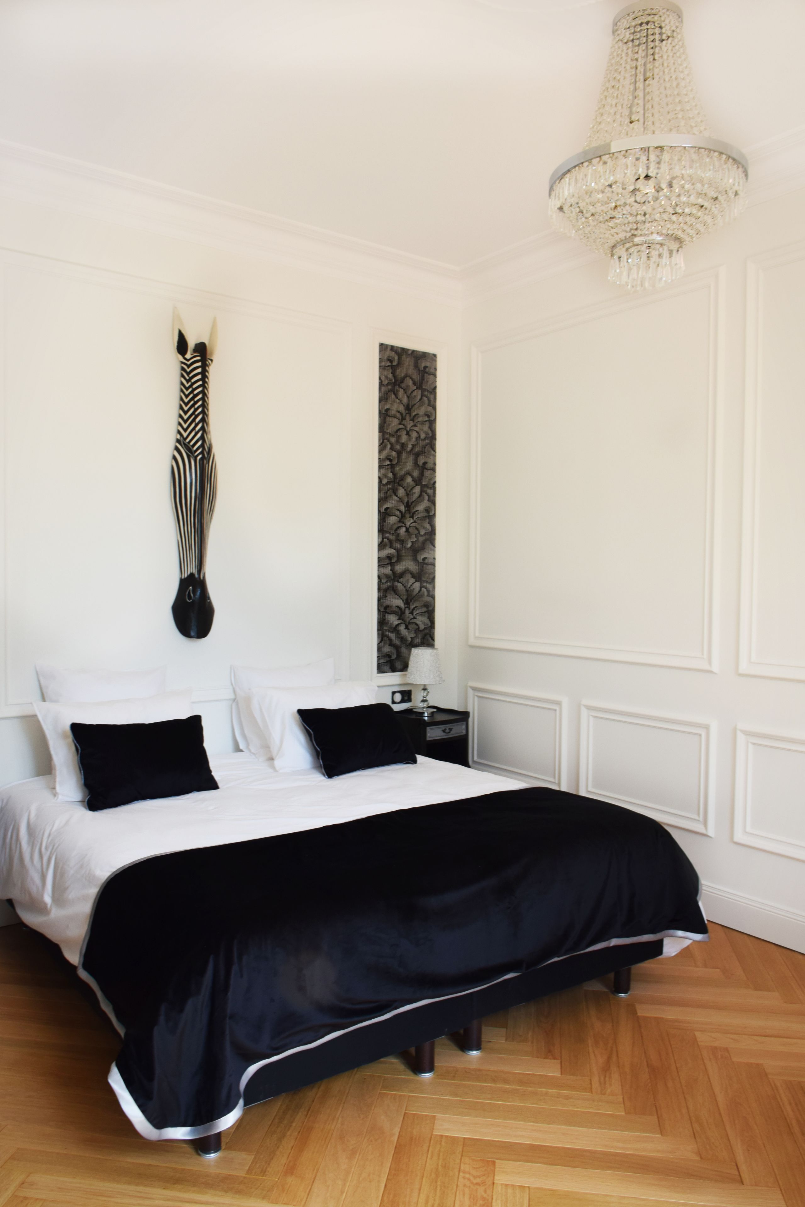 Un dormitorio con una cama grande, una araña, un relieve decorativo de cabeza de cebra en la pared y un panel de papel tapiz estampado.