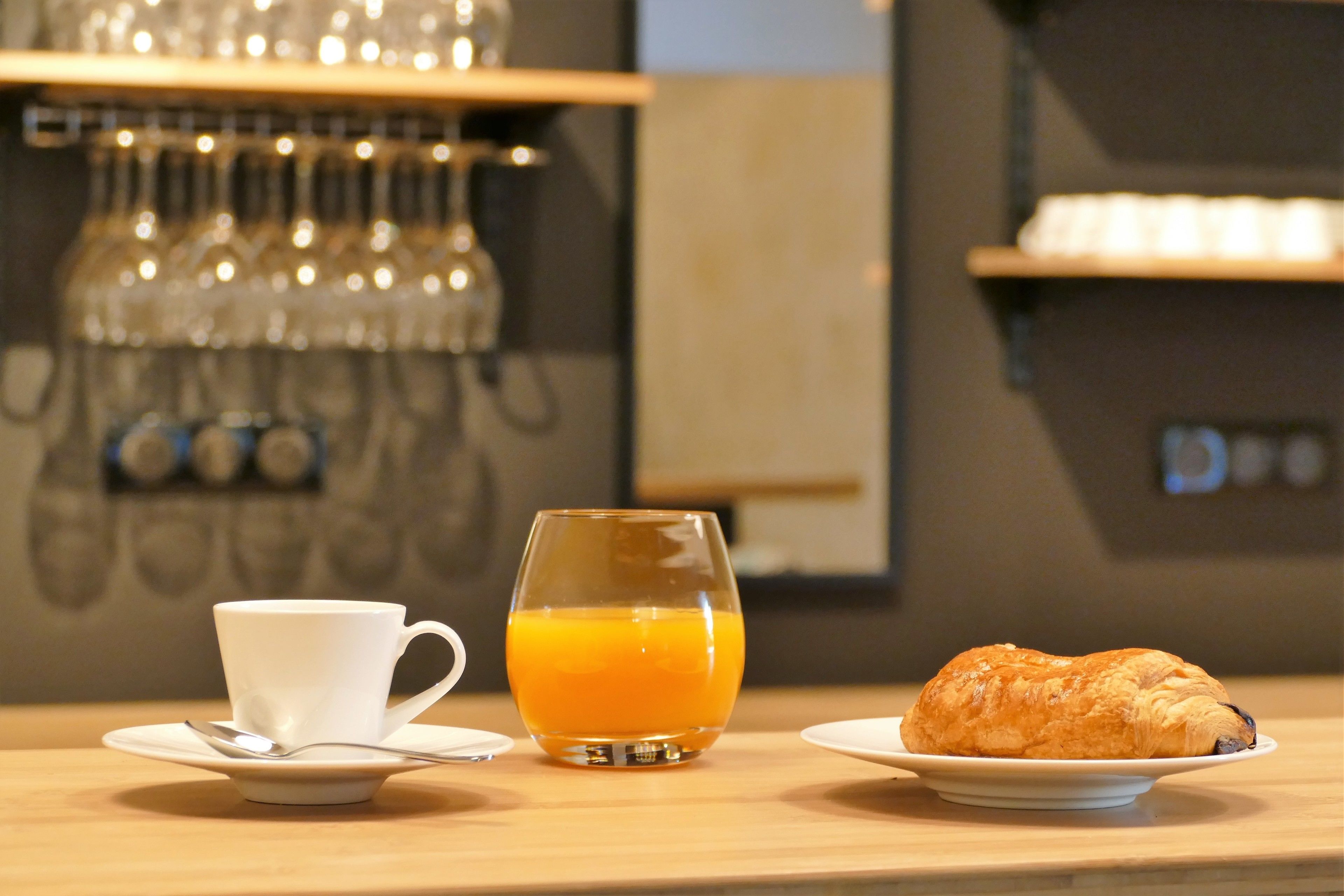 Un desayuno con una taza, un vaso de zumo de naranja y un croissant sobre una mesa de madera.