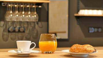 Un desayuno con una taza, un vaso de zumo de naranja y un croissant sobre una mesa de madera.