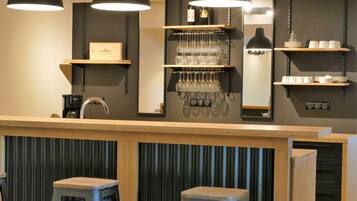 A bar area with stools, shelves holding glasses and bottles, and a coffee machine.